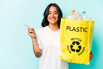 Young hispanic woman recycling plastic isolated on yellow background smiling and pointing aside, showing something at blank space.