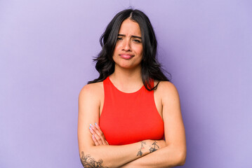 Young hispanic woman isolated on purple background frowning face in displeasure, keeps arms folded.