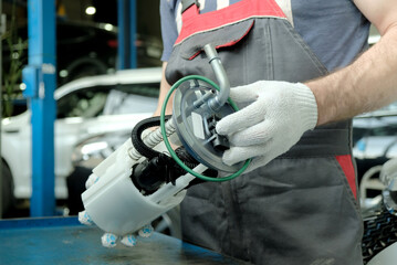 Car maintenance at a car service. An auto mechanic holds a new fuel pump in his hands. Repair of the fuel and exhaust system of the car.