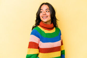 Young hispanic woman isolated on yellow background looks aside smiling, cheerful and pleasant.