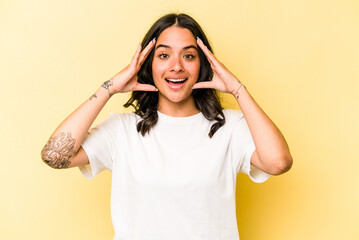 Young hispanic woman isolated on yellow background receiving a pleasant surprise, excited and raising hands.