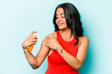 Young hispanic woman holding sun cream isolated on blue background