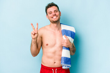 Fototapeta premium Young caucasian man holding beach towel isolated on blue background showing number two with fingers.