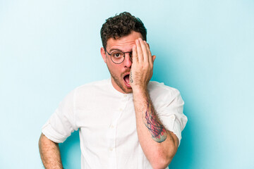 Young caucasian man isolated on blue background having fun covering half of face with palm.