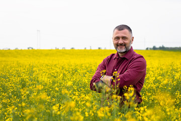 Portrait of smiling middle age farmer standing in rapeseed field examining crop.