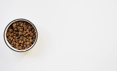 Top view on bowl with healthy dry pet food on light background. Copy space. Animal care, animal friendly concept. Cat food. Tasty and crunchy pieces of food.