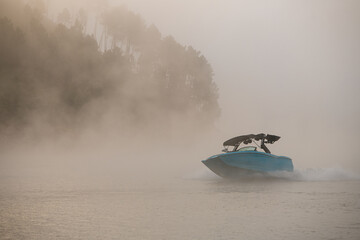 picturesque view on boat quickly floating on the water against the backdrop of silhouette of hill in fog