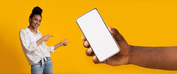 Black lady pointing at white empty smartphone screen, mockup - obrazy, fototapety, plakaty