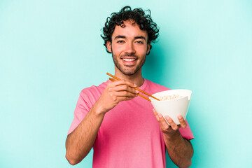 Young caucasian man eating noodles isolated on blue background