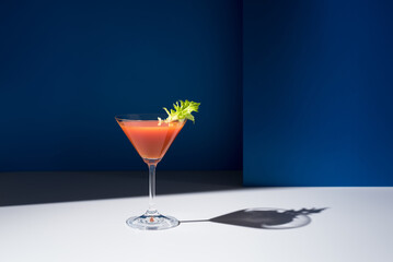 Bloody Mary decorado con hoja de apio en copa de cóctel sobre fondo azul