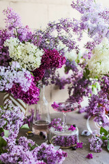 A carbonated lilac cocktail in a wide glass on the table among a huge amount of lilacs.