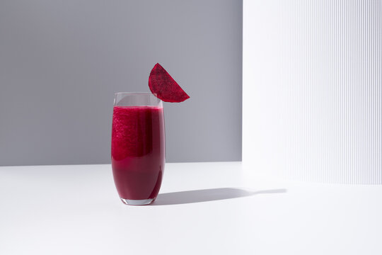 Un vaso de jugo de remolacha decorado con rodaja de remolacha sobre una mesa blanca y fondo gris	