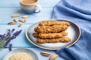 Crumble cookies with seasme and almonds on ceramic plate with cup of coffee on blue wooden background. side view, close up.
