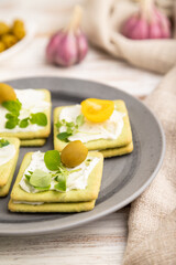 Green cracker sandwiches with cream cheese and cherry tomatoes on white wooden background. side view, selective focus.