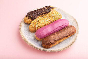 Set of eclair, traditional french dessert on ceramic plate on pink pastel background. side view, close up.