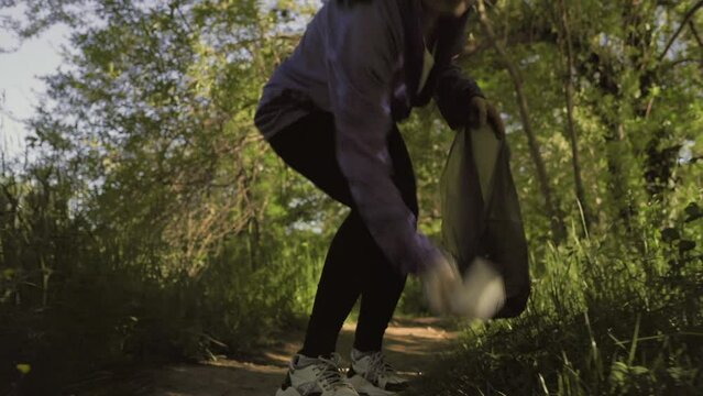 A young woman runs through the forest and collects garbage in the forest. Low angle view. The concept of plogging and environmental cleaning.