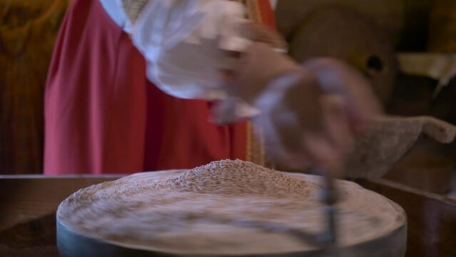 Woman in traditional Russian style costume is grinding flour in vintage stone mill