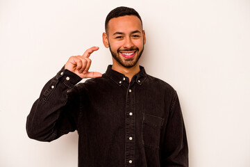 Young hispanic man isolated on white background holding something little with forefingers, smiling and confident.