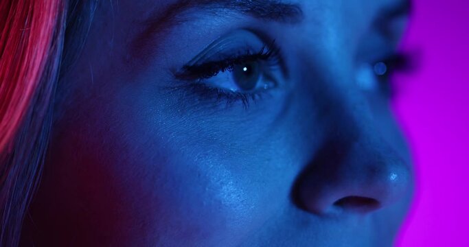 Close-up eyes of young beautiful girl closing and opening eyes, looking away on purple background in neon light. Concept of beauty, vision, makeup youth, art. 4k