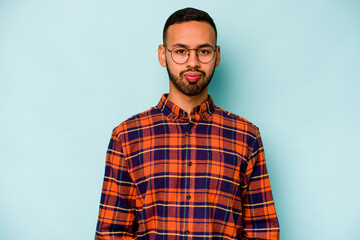 Young hispanic man isolated on blue background blows cheeks, has tired expression. Facial expression concept.