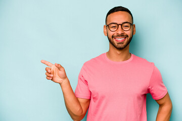 Young hispanic man isolated on blue background smiling cheerfully pointing with forefinger away.