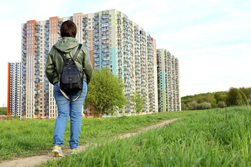 Woman looks at the new houses walking on green  path, ecologically clean district. Building industry and real estate concept