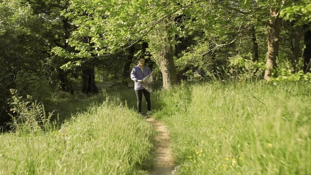 A young happy woman jogging at the park and collects garbage. Follow shot. The concept of plogging and environment protection.