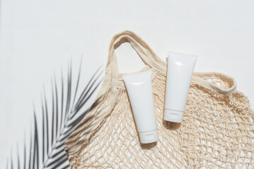 Plastic white tubes for cream or lotion and cloth shopping bag. Sunscreen cosmetic on white...