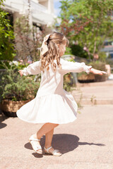 A charming little girl with long blond hair playing against the background of nature. A happy child enjoys summer time in the Park