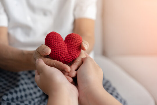 Young and senior woman holding each other hands and red yarn heart shape togetherness concept. Elderly care and protection with love from grandchild.