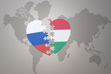 puzzle heart with the national flag of russia and hungary on a world map background. Concept.