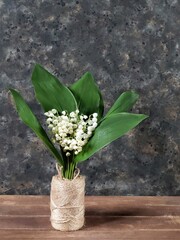 Bouquet of lilies of the valley in skein of twine on wooden rustic table on black concrete background with copy space. Bridal greeting card. Still life with spring flowers.