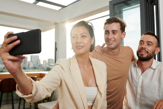 Smiling woman taking selfie with friends in rooftop bar