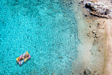 A woman in bikini on a float enjoys the turquoise waters of the Aegean Sea in Greece during summer time