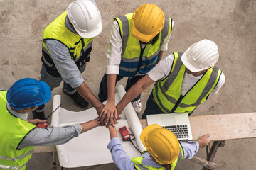 team of male and female engineers and contractors look at blueprints and join hand together at the...