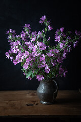 Malva sylvestris in an old vase on the dark background.  Common mallow (Malva sylvestris) flowers.