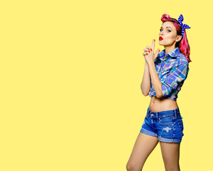 Pin up girl. Portrait of red purple attractive woman showing hand sign gesture. Retro and vintage concept. Yellow background with copy space text area. Pinup female model pose at studio.