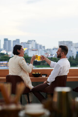 Friends toasting with beer mugs when resting in rooftop bar with beautiful view