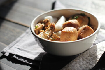 Rolled Rice Noodles in Five-spices Broth served in a white cup on a black wooden table.