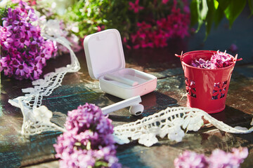  Aesthetic lifestyle flat lay, wireless headphones, lilac flowers and lace decorations. Listening music or audiobook, taking webinar or online chat, speaking by phone on sunny garden.