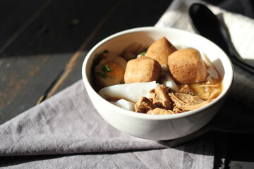 Thai food, Chinese roll noodle soup served in a white cup on a black wooden table.
