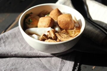 Thai food, Chinese roll noodle soup served in a white cup on a black wooden table.