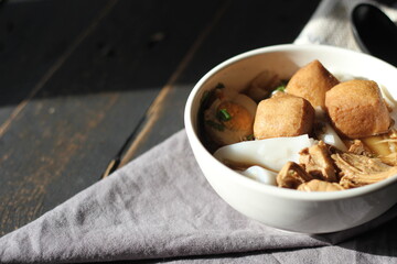 Thai food, Chinese roll noodle soup served in a white cup on a black wooden table.