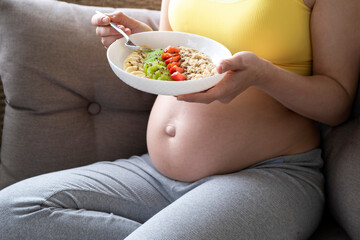 Belly of pregnant woman and plate with oatmeal and fruits. Nutrition and healthy diet during...