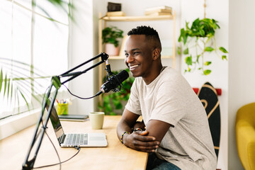 Happy young african man making audio podcast from home - Content creator recording radio show using...