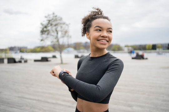 A smart watch with a pulse and a cardio machine is used by a female trainer who trains outside in sports clothes.
