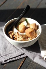 Rolled Rice Noodles in Five-spices Broth served in a white cup on a black wooden table.
