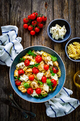 Roasted chicken nuggets, cherry tomatoes, feta cheese and fusilli  served on wooden table
