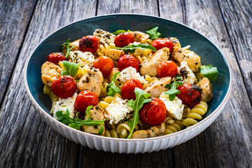 Roasted chicken nuggets, cherry tomatoes, feta cheese and fusilli  served on wooden table
