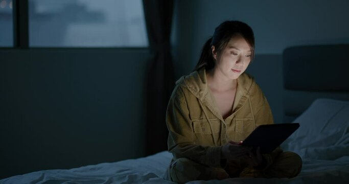 Woman watch on tablet computer and sit on bed at night